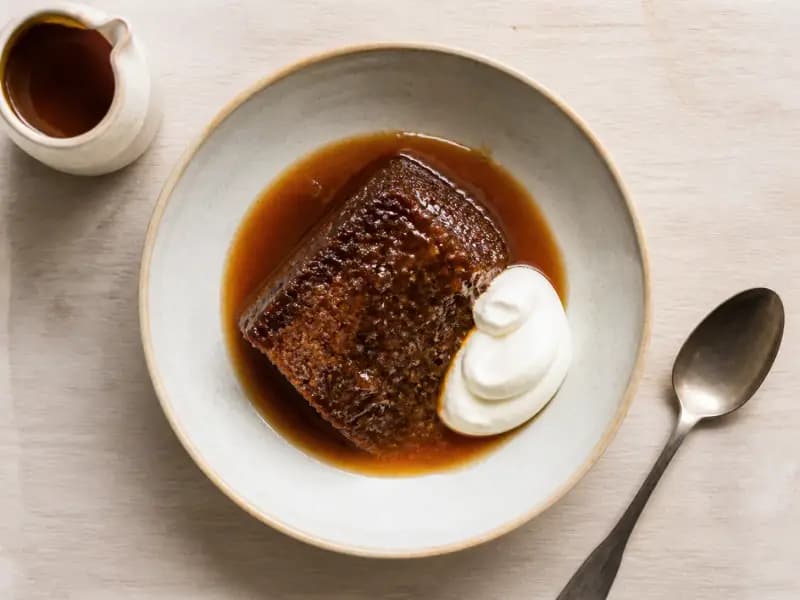 Sticky Toffee Pudding — shot from directly overhead: a dark date sponge skewered and soaked with hot toffee sauce the moment it leaves the oven