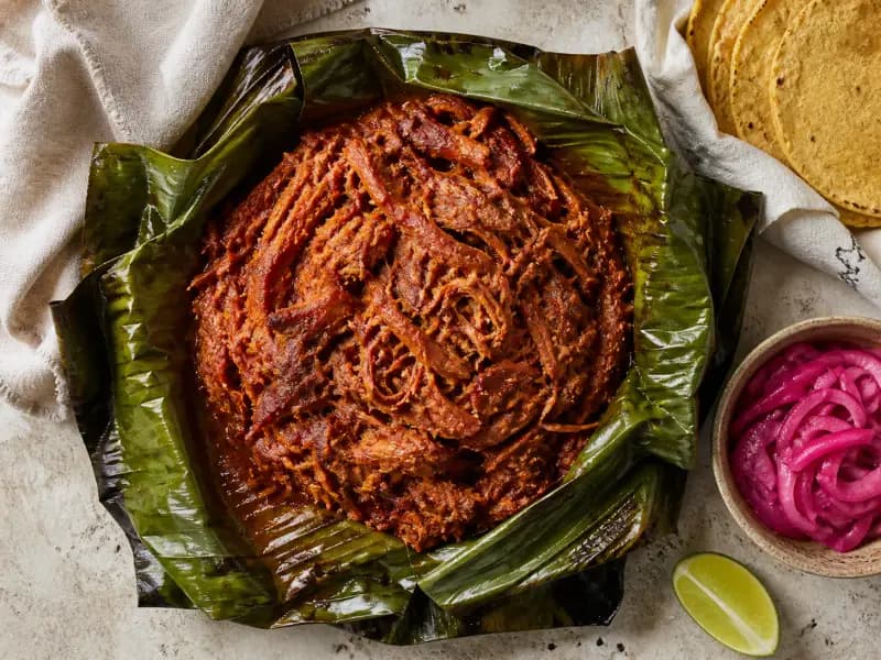 Cochinita Pibil — shot from directly overhead: pork buried in achiote and sour orange
